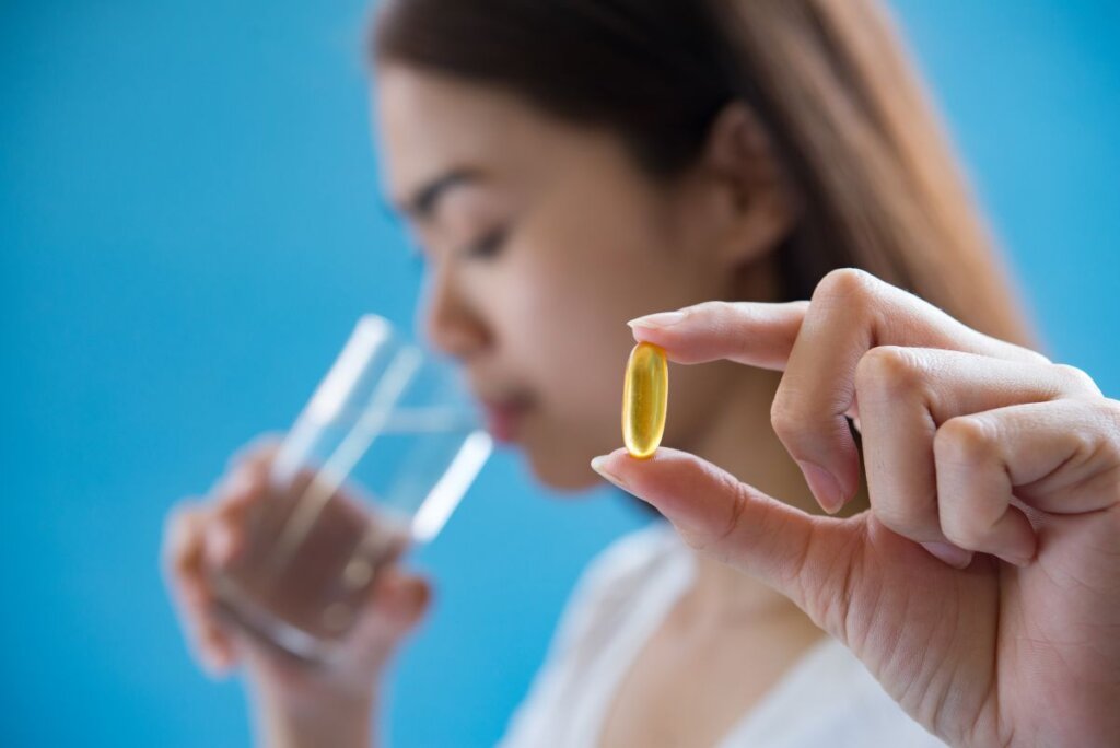 Mujer sosteniendo una cápsula de omega 3 y un vaso de agua, representando el consumo de suplementos nutricionales para cuidar la salud del corazón, el cerebro y el bienestar general.