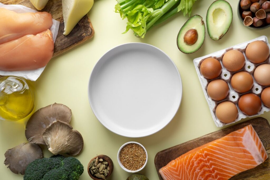 Plato con espinacas frescas, huevos cocidos y medio aguacate acompañado de aceite de oliva sobre una mesa clara, alimentos representativos de la dieta cetogénica por su alto contenido en grasas saludables y bajo nivel de carbohidratos.