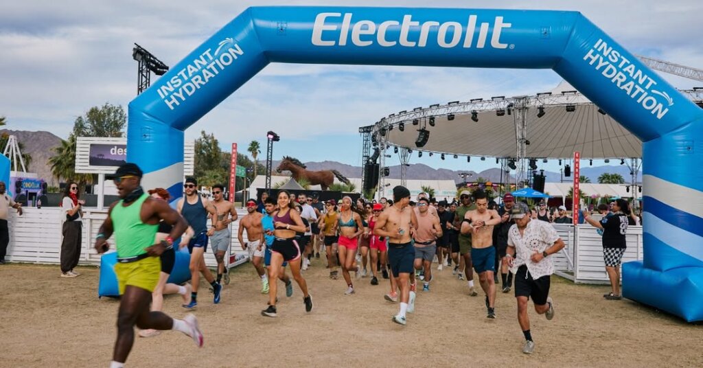 Corredores participan en una activación deportiva patrocinada por Electrolit, bajo un arco inflable con el lema Instant Hydration, durante un evento masivo que combina deporte, música y estilo de vida saludable.