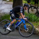Edgar Cadena compite en una prueba de ciclismo de ruta sobre una bicicleta azul, con casco y uniforme negro.